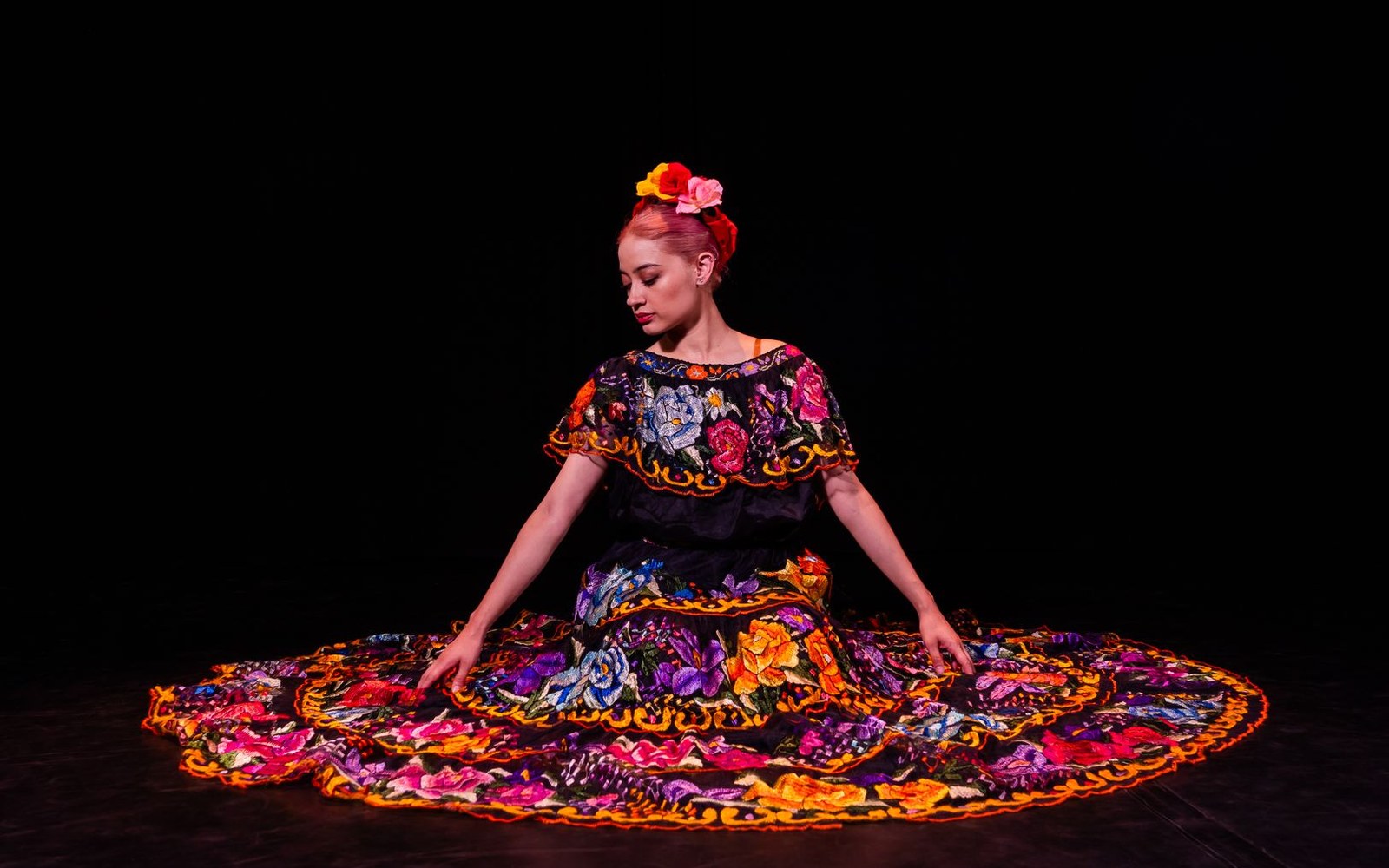 Dancer in floral embroidered Mexican folklórico dress spreads its wide skirt on stage
