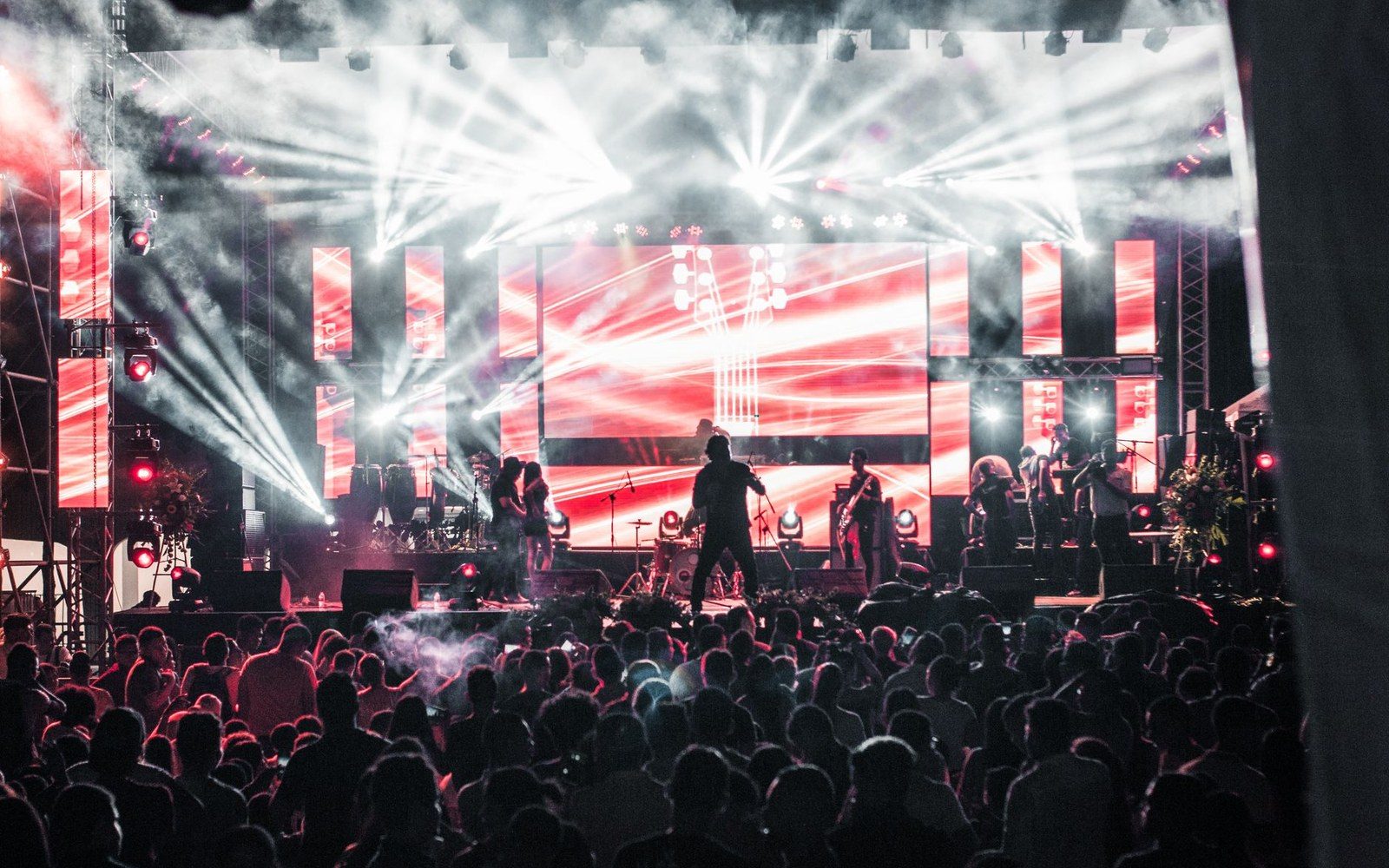 Band performs on a red and white lit stage in front of a large crowd