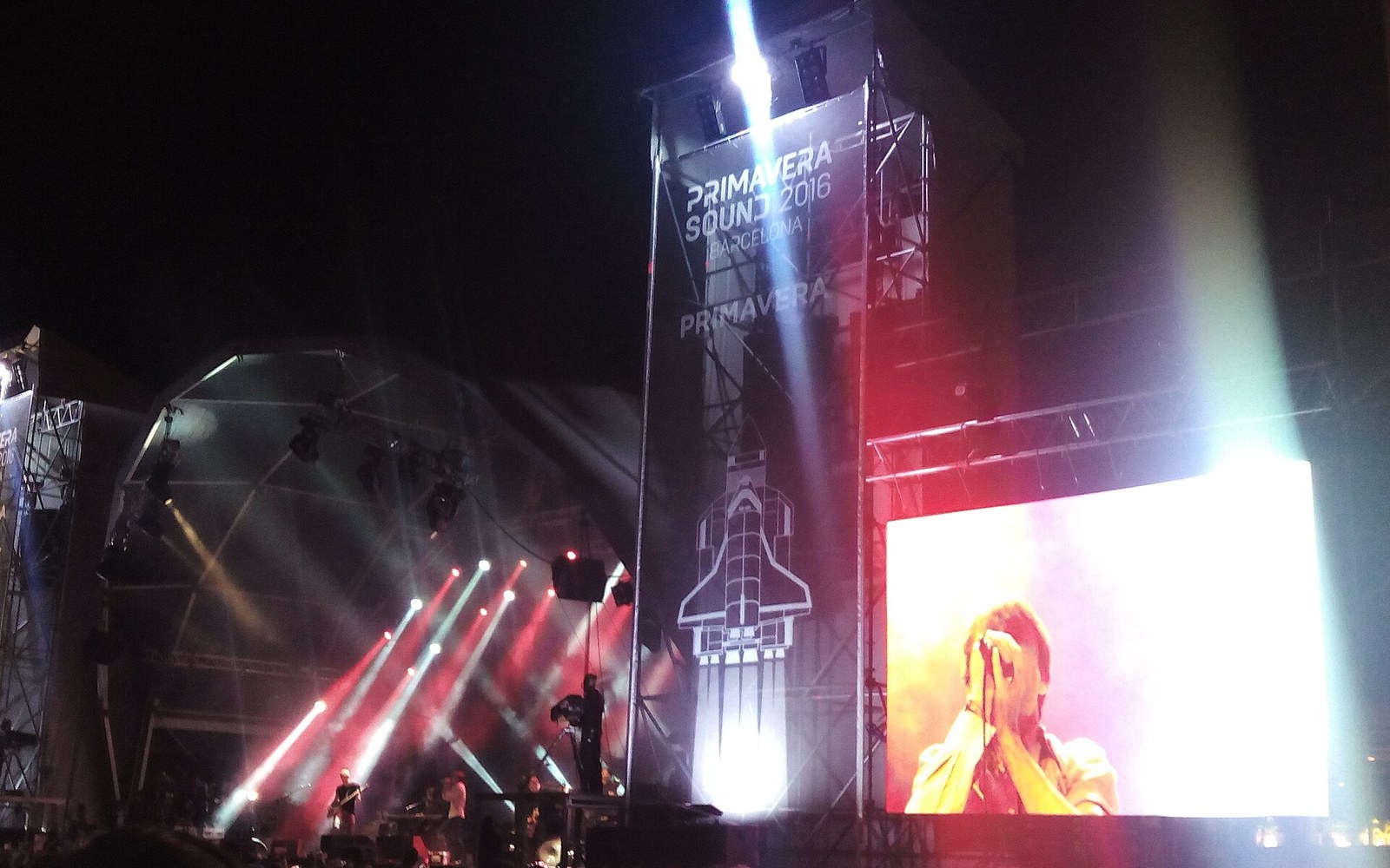Concert stage lit with red beams and a large screen showing a singer performing