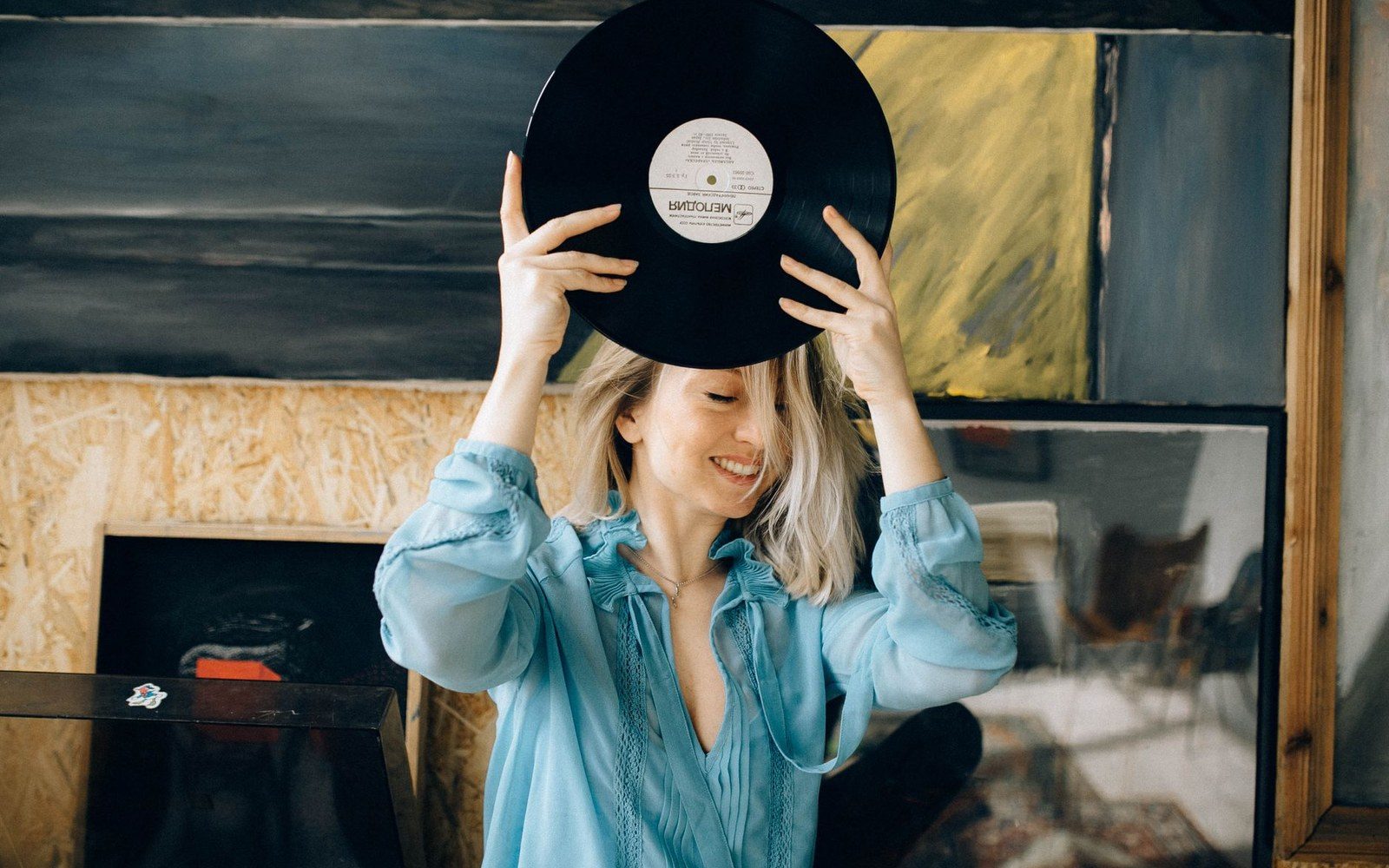 Smiling woman in a blue blouse holds a vinyl record above her head