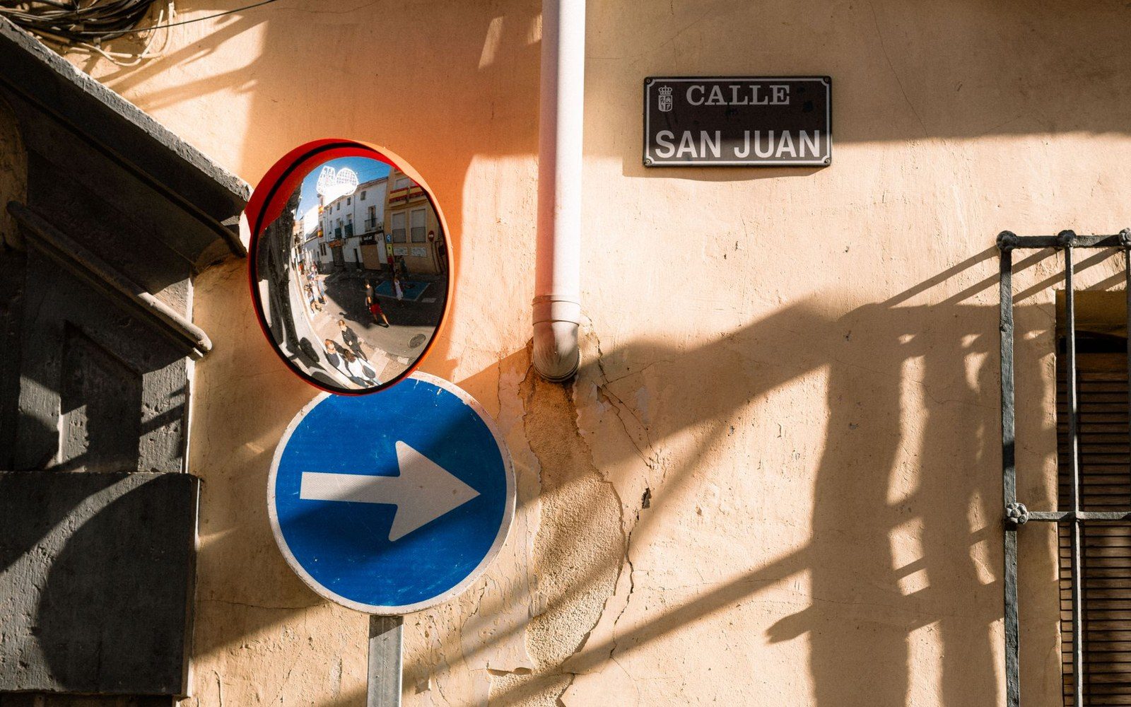 Traffic mirror and blue arrow sign beside a Calle San Juan street nameplate