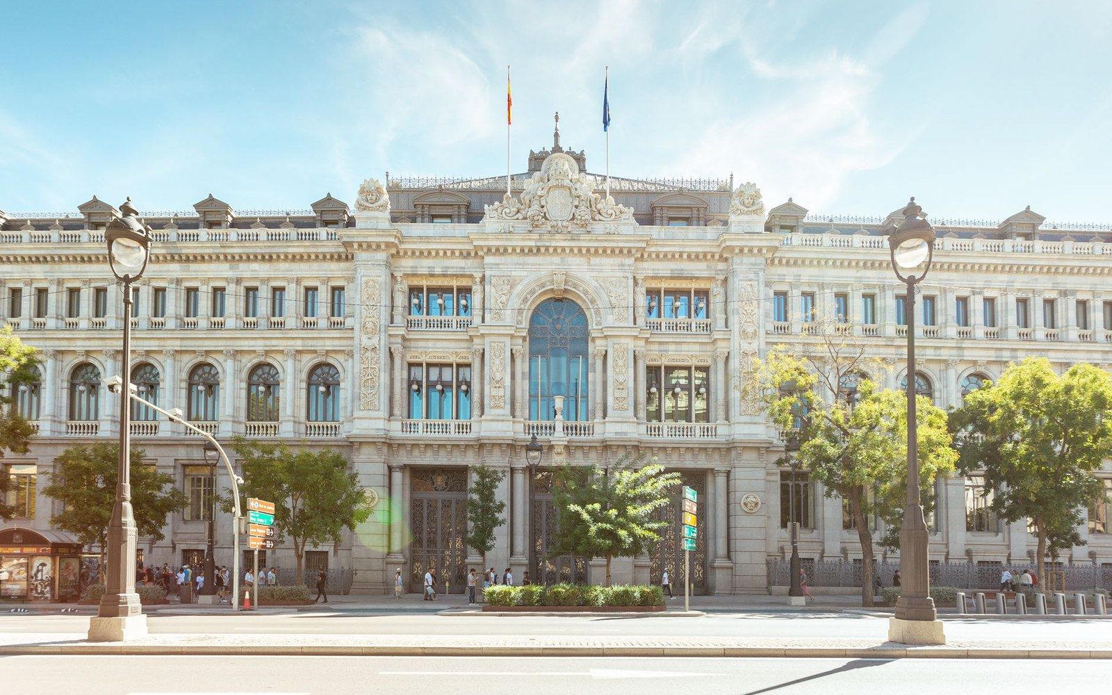Ornate stone facade of a historic building with flagpoles and street lamps in front