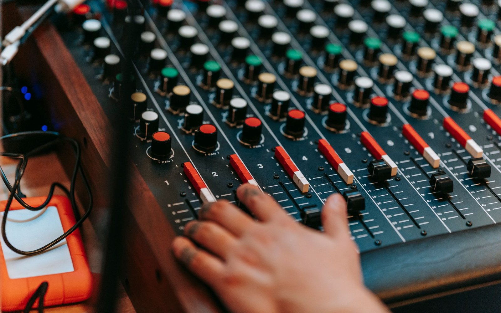 Studio mixing desk with all faders raised, engineer's hands visible at the board